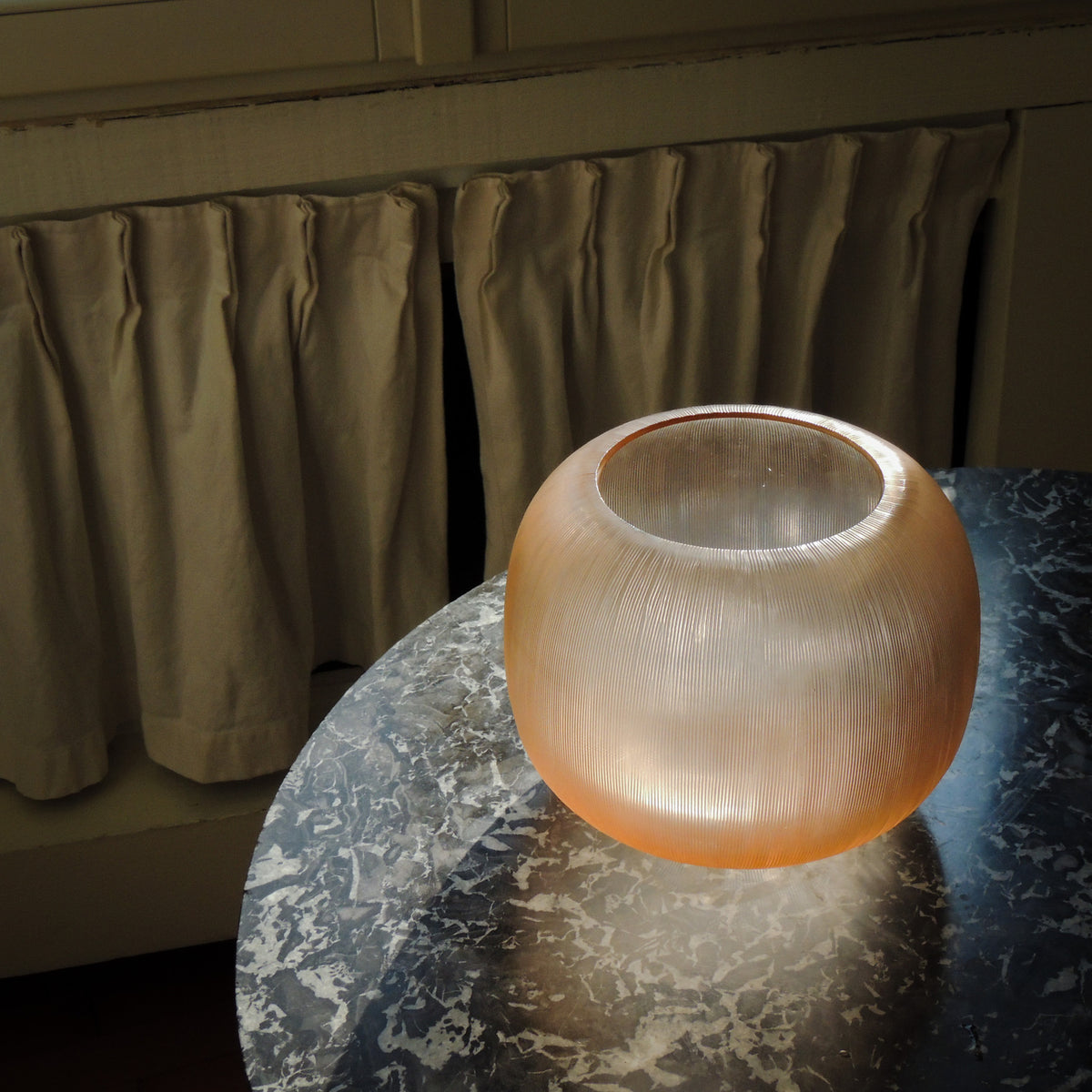 Riccio Rosé Millerighe vase, round Murano glass vase in soft peach-pink with fine vertical lines, glowing in the light on a marble table